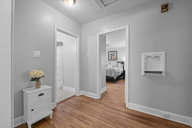 corridor featuring baseboards, light wood finished floors, and attic access