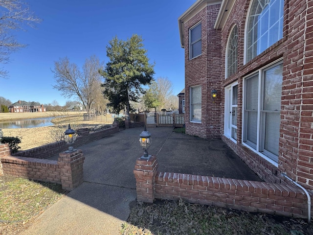 exterior space featuring a water view, a patio area, a gate, fence, and brick siding
