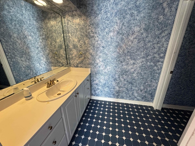 bathroom featuring baseboards, vanity, and wallpapered walls