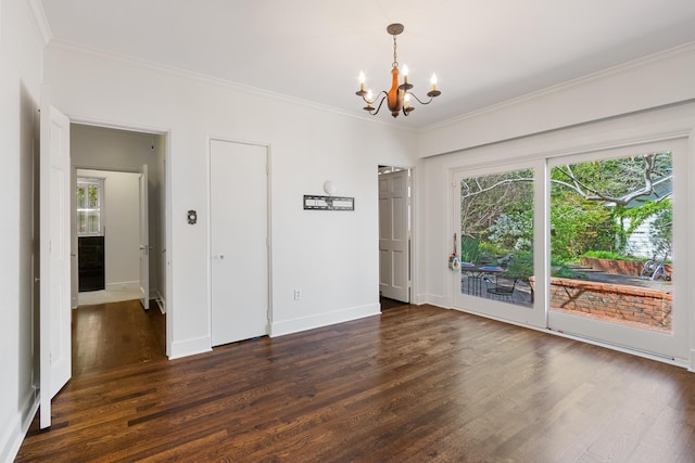 empty room featuring crown molding, dark wood finished floors, an inviting chandelier, and a healthy amount of sunlight