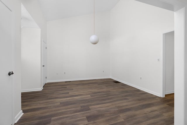 spare room with vaulted ceiling, dark wood-type flooring, and baseboards