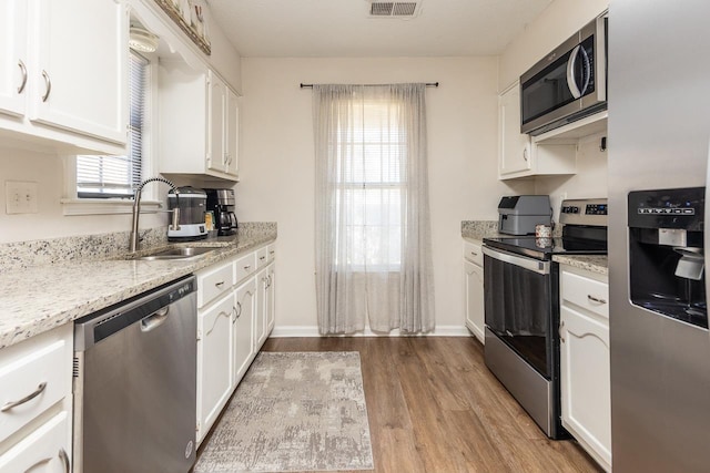 kitchen featuring light wood-style flooring, white cabinetry, light stone countertops, stainless steel appliances, and a sink