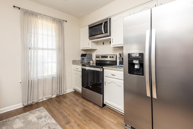 kitchen with a textured ceiling, white cabinets, stainless steel appliances, light wood finished floors, and baseboards