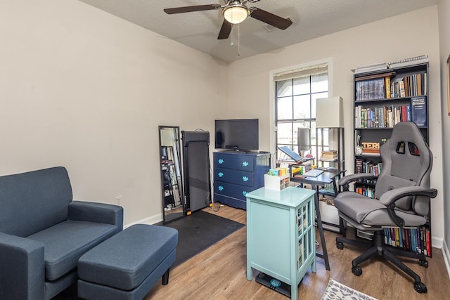office space featuring light wood-style flooring, a ceiling fan, baseboards, and a textured ceiling