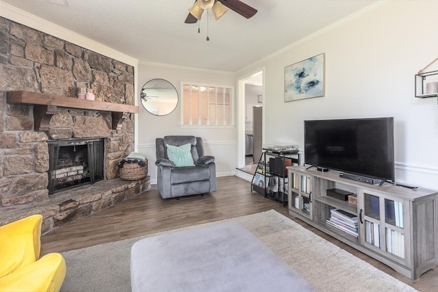 living area with a ceiling fan, a textured ceiling, crown molding, a fireplace, and wood finished floors