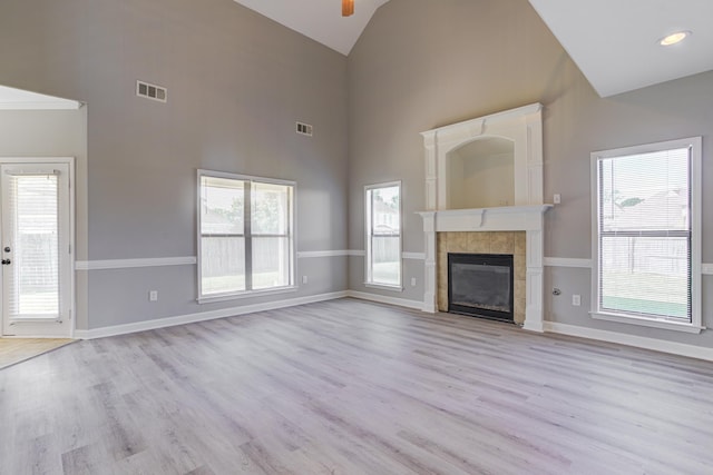 unfurnished living room featuring a tiled fireplace, visible vents, light wood-style flooring, and ceiling fan