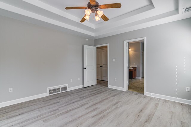 unfurnished bedroom featuring visible vents, baseboards, a tray ceiling, and light wood-style floors
