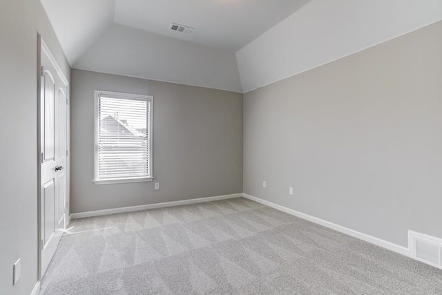 empty room with light carpet, visible vents, baseboards, and vaulted ceiling
