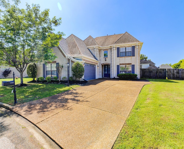 traditional-style home featuring an attached garage, driveway, fence, and a front lawn