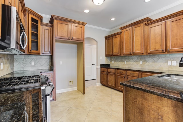 kitchen featuring baseboards, arched walkways, brown cabinetry, recessed lighting, and stainless steel appliances