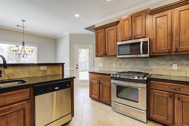 kitchen featuring dark stone counters, a sink, stainless steel appliances, a notable chandelier, and backsplash