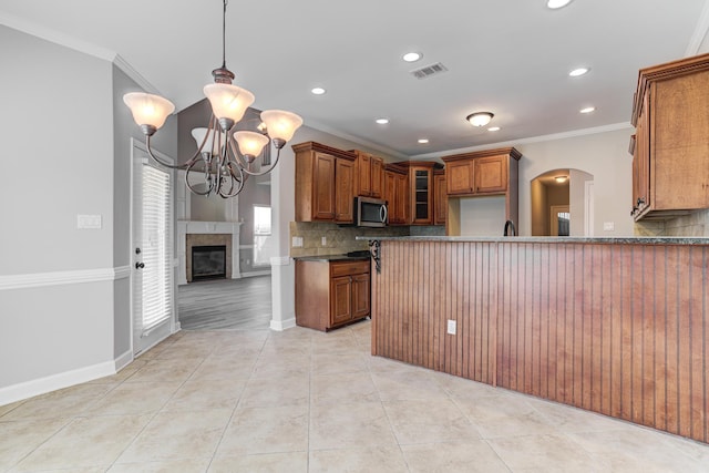 kitchen with tasteful backsplash, a notable chandelier, ornamental molding, stainless steel microwave, and brown cabinetry