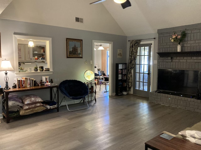 living room featuring a brick fireplace, wood finished floors, baseboards, ceiling fan, and high vaulted ceiling
