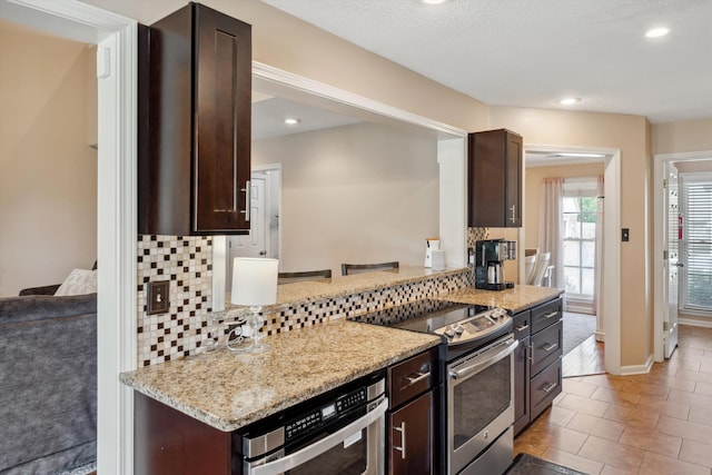 kitchen with appliances with stainless steel finishes, light stone counters, backsplash, and dark brown cabinetry