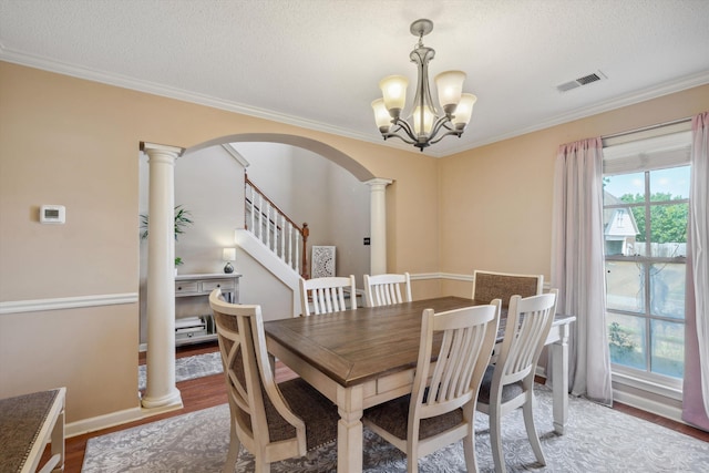dining area featuring an inviting chandelier, visible vents, ornate columns, arched walkways, and wood finished floors