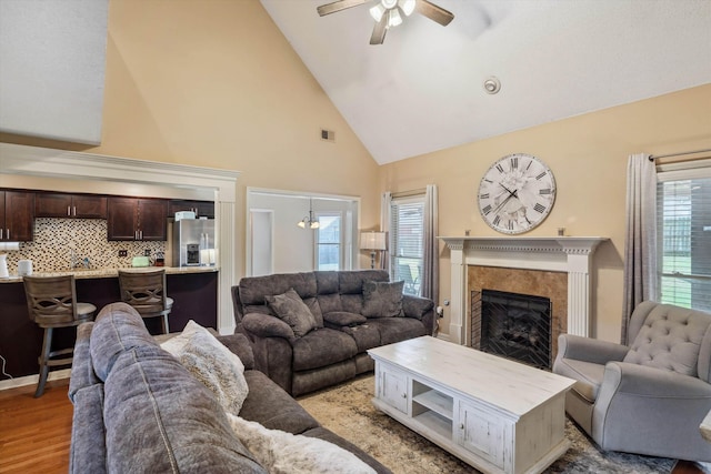 living room featuring a fireplace, visible vents, ceiling fan, high vaulted ceiling, and light wood finished floors