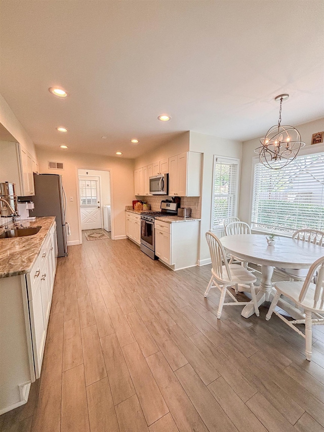 kitchen with independent washer and dryer, visible vents, a sink, stainless steel appliances, and light wood finished floors