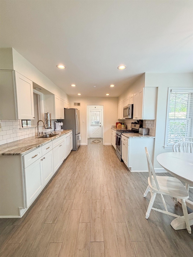 kitchen featuring light wood-style floors, light stone countertops, white cabinets, appliances with stainless steel finishes, and a sink