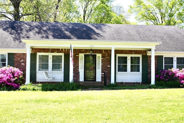 single story home featuring a porch, brick siding, a shingled roof, and a front yard
