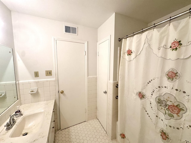 full bathroom featuring vanity, a wainscoted wall, visible vents, and tile walls