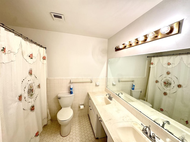 full bath with a sink, tile walls, toilet, and visible vents