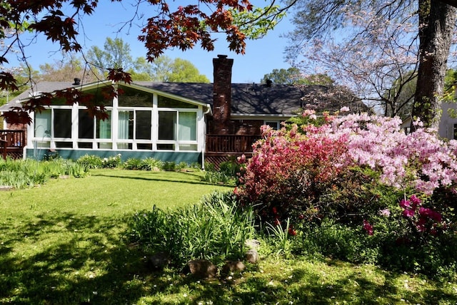rear view of house with a sunroom, a wooden deck, a yard, and a chimney