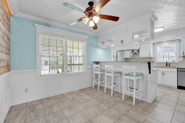 kitchen featuring a sink, white cabinets, a breakfast bar, and wainscoting