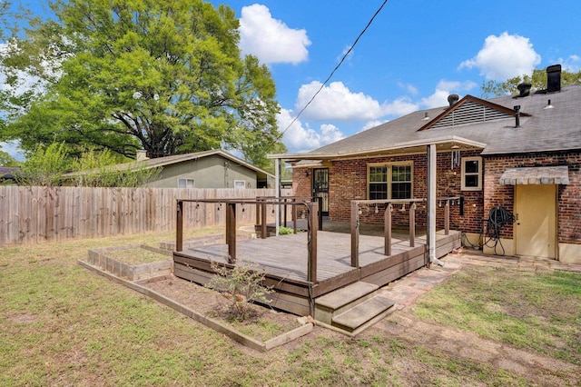 back of house with a lawn, a garden, fence, brick siding, and a deck