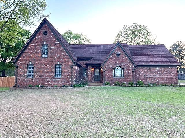 view of front facade with brick siding, a front lawn, and a tiled roof