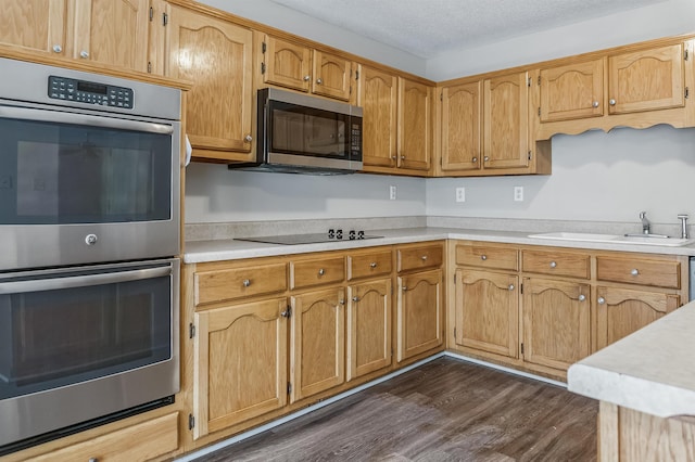 kitchen with a textured ceiling, dark wood-style flooring, light countertops, a sink, and stainless steel appliances