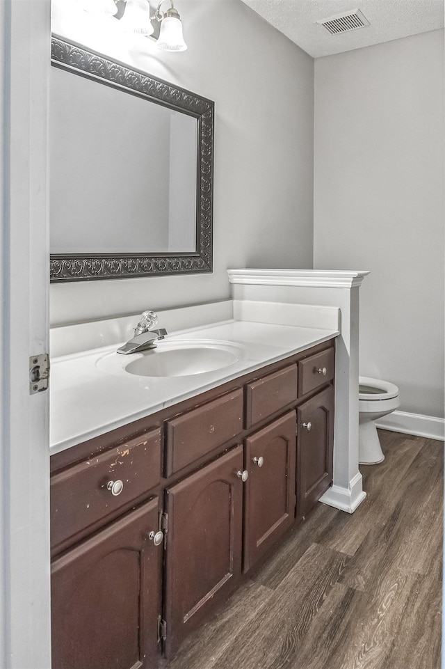 bathroom with vanity, a textured ceiling, toilet, visible vents, and wood finished floors