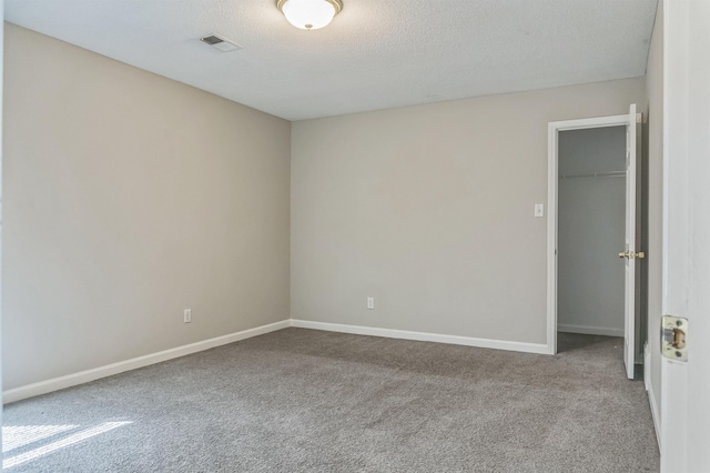unfurnished bedroom with visible vents, baseboards, a textured ceiling, carpet floors, and a walk in closet