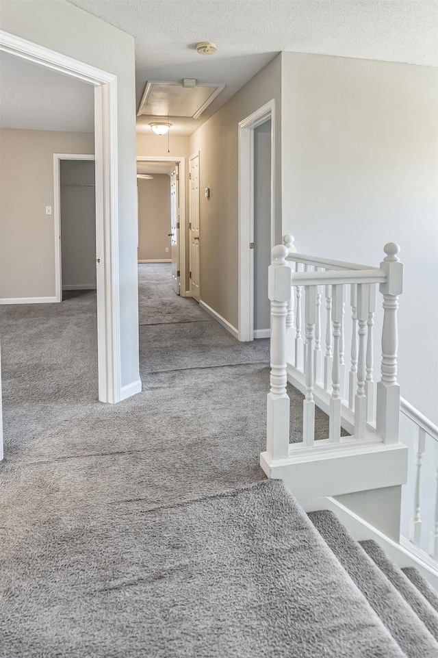 corridor with carpet, a textured ceiling, attic access, an upstairs landing, and baseboards