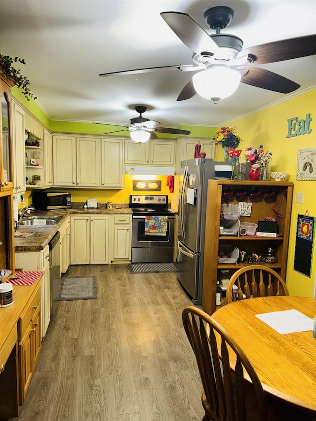 kitchen with appliances with stainless steel finishes, cream cabinetry, ceiling fan, a sink, and wood finished floors