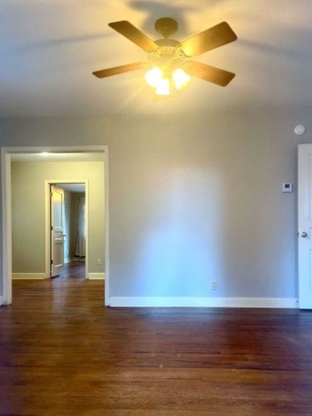 spare room with dark wood-style flooring, a ceiling fan, and baseboards