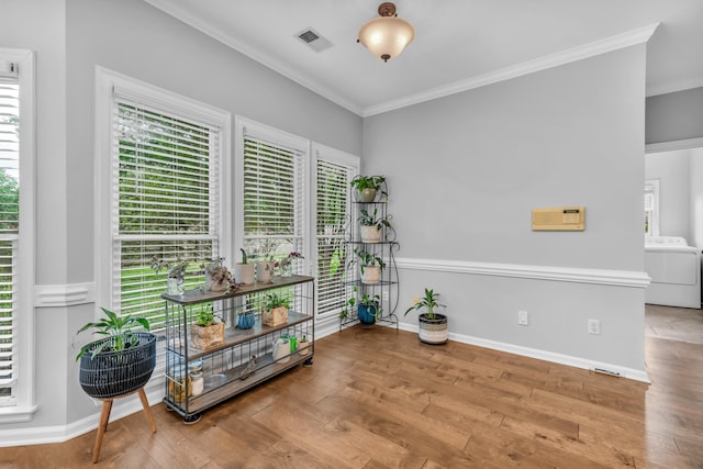 living area featuring wood finished floors, washer / dryer, ornamental molding, baseboards, and visible vents
