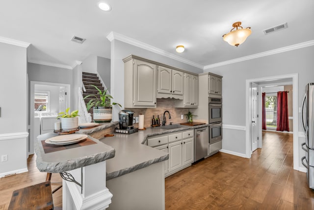 kitchen featuring a sink, stainless steel appliances, washer and clothes dryer, visible vents, and a peninsula