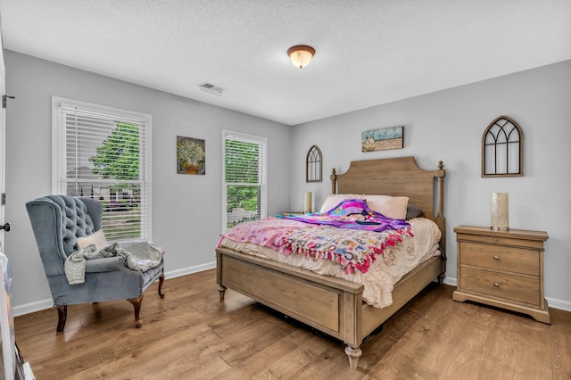 bedroom featuring a textured ceiling, visible vents, wood finished floors, and baseboards