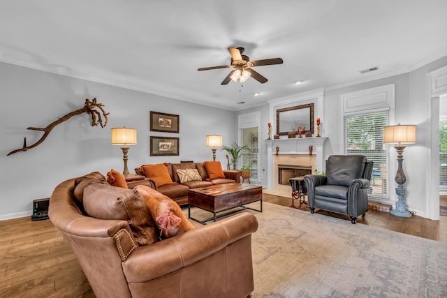 living room featuring a ceiling fan, visible vents, baseboards, ornamental molding, and wood finished floors