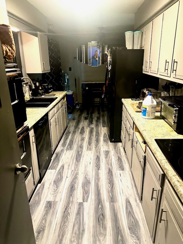 kitchen with a sink, a toaster, light wood-style flooring, white cabinetry, and black appliances