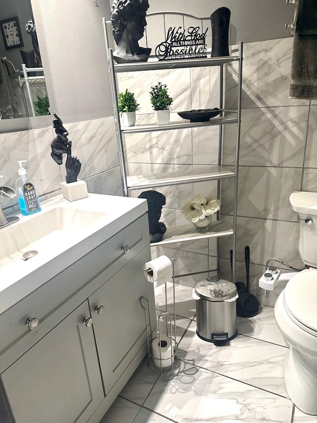 bathroom featuring toilet, marble finish floor, vanity, and tile walls