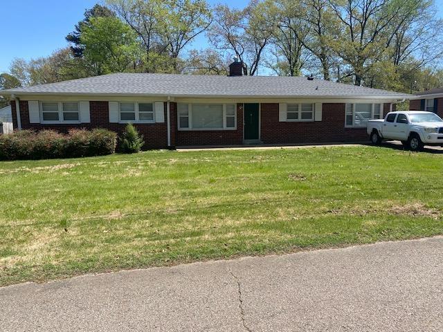 single story home with a chimney, a front yard, and brick siding