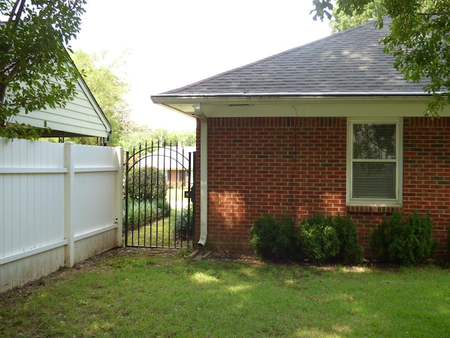 view of property exterior with a gate, brick siding, a shingled roof, fence, and a lawn