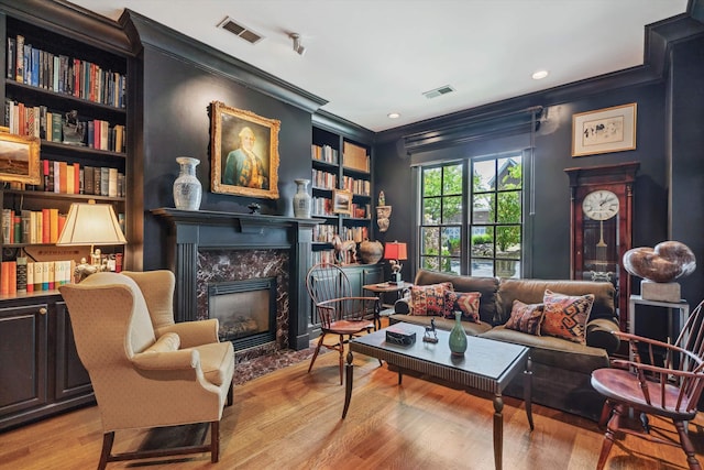 sitting room featuring wood finished floors, visible vents, crown molding, and a premium fireplace
