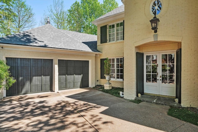 exterior space featuring brick siding, an attached garage, french doors, a shingled roof, and concrete driveway