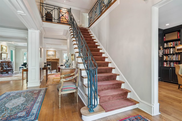 stairs featuring decorative columns, wood finished floors, built in features, and crown molding