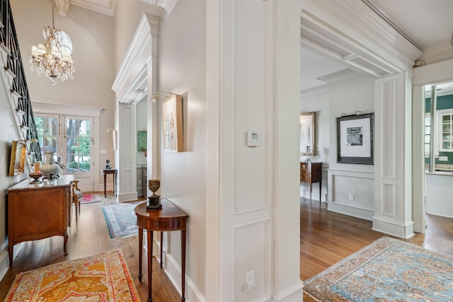 hallway featuring a chandelier, wood finished floors, a decorative wall, and ornamental molding