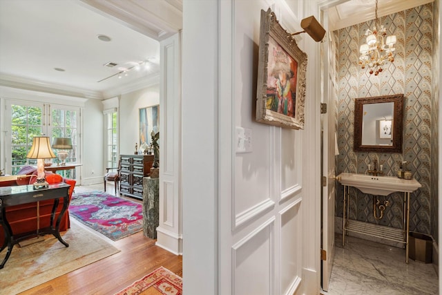 corridor with a notable chandelier, ornamental molding, visible vents, a sink, and wood finished floors