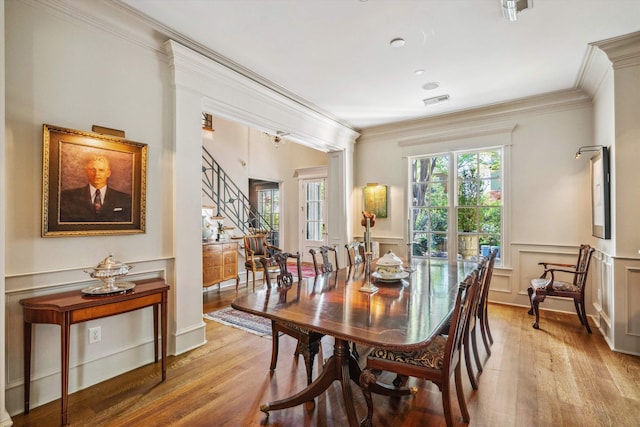 dining room with ornamental molding, a wainscoted wall, visible vents, a decorative wall, and light wood finished floors