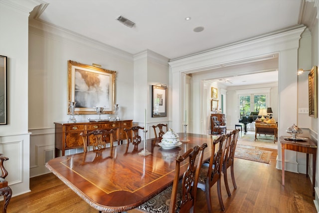 dining room featuring crown molding, visible vents, a wainscoted wall, and wood finished floors